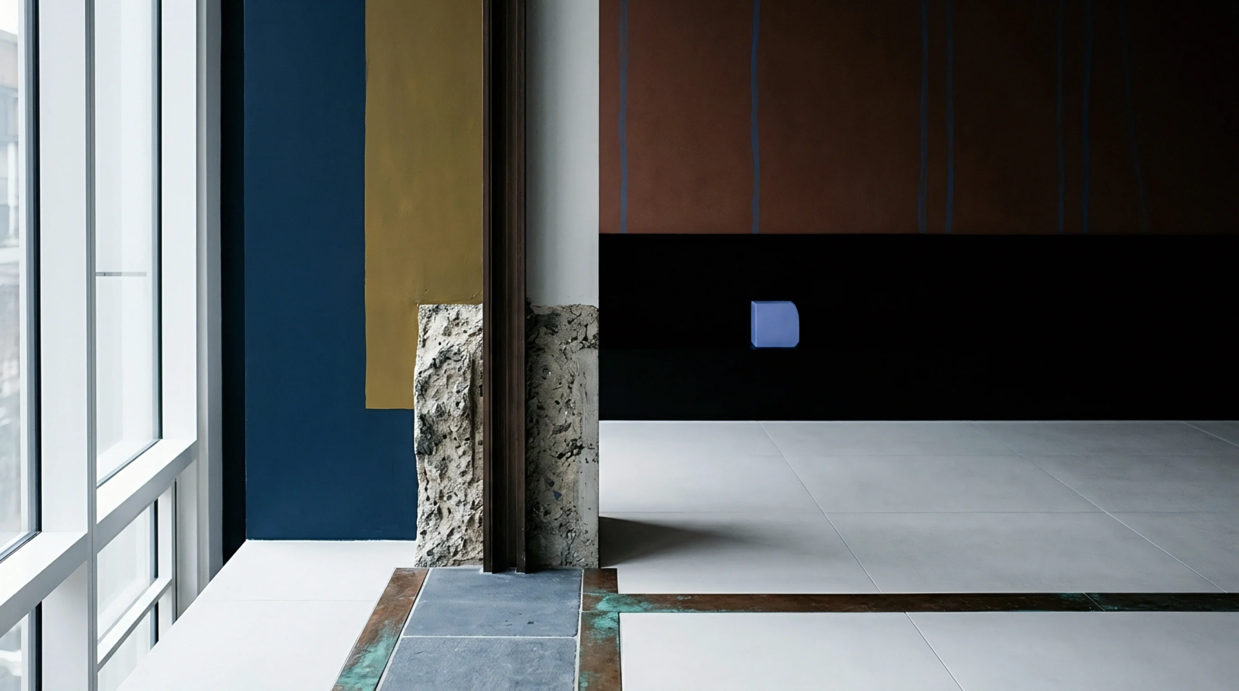 Structural concrete columns divide a workspace featuring segmented floor tiles and metallic inlay borders against multicolored vertical wall panel sections.