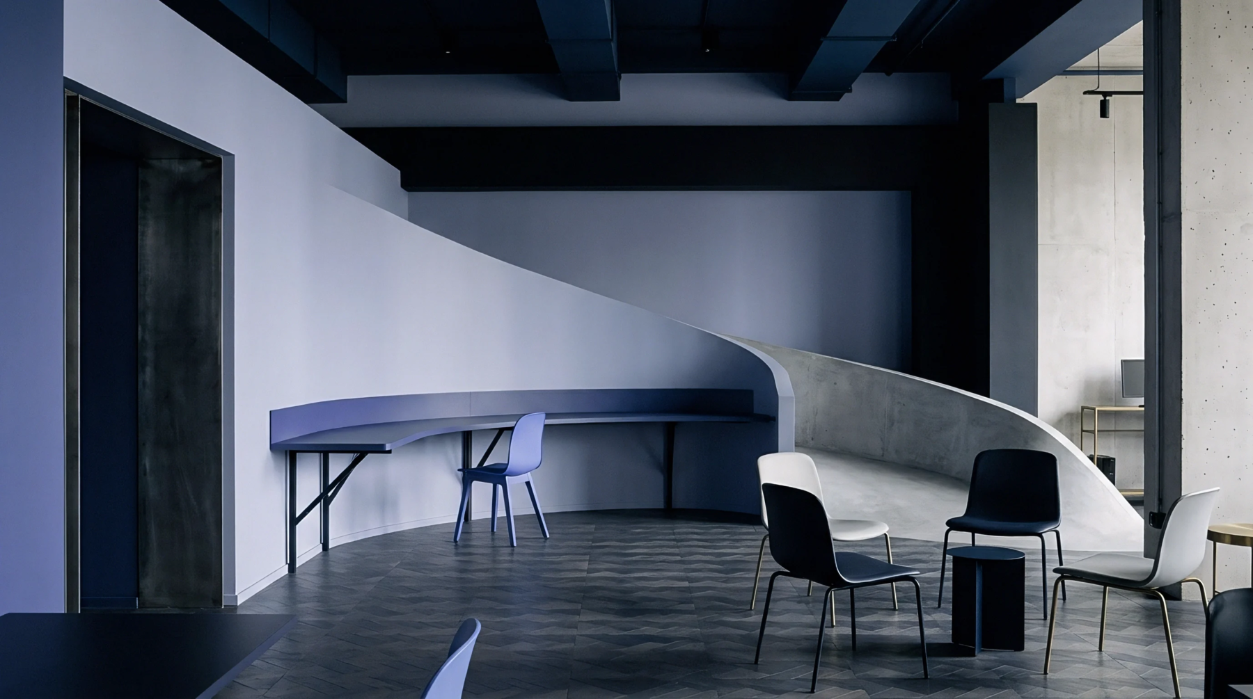 An industrial design studio features a sweeping concrete ramp, a contoured perimeter desk, and grouped chairs on a dark wood floor.