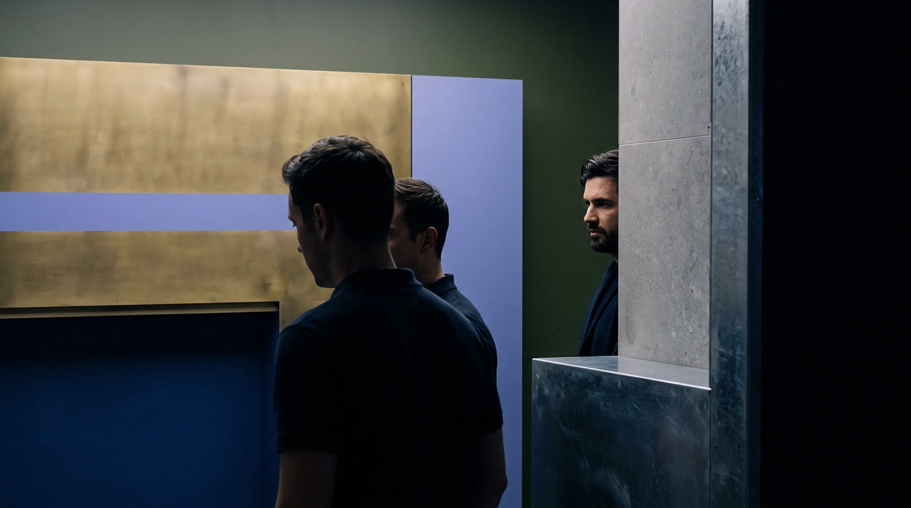 Three men in dark shirts are positioned within a minimalist interior featuring metallic and colored wall panels and a concrete pillar.